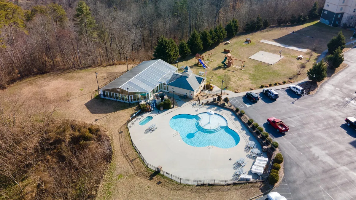 This image captures the vibrant outdoor swimming pool area surrounded by a recreational zone and the lodge building, framed by lush trees. The pool features inviting blue water and a spacious deck, creating a lively, family-friendly atmosphere ideal for swimming, sunbathing, and children's play.