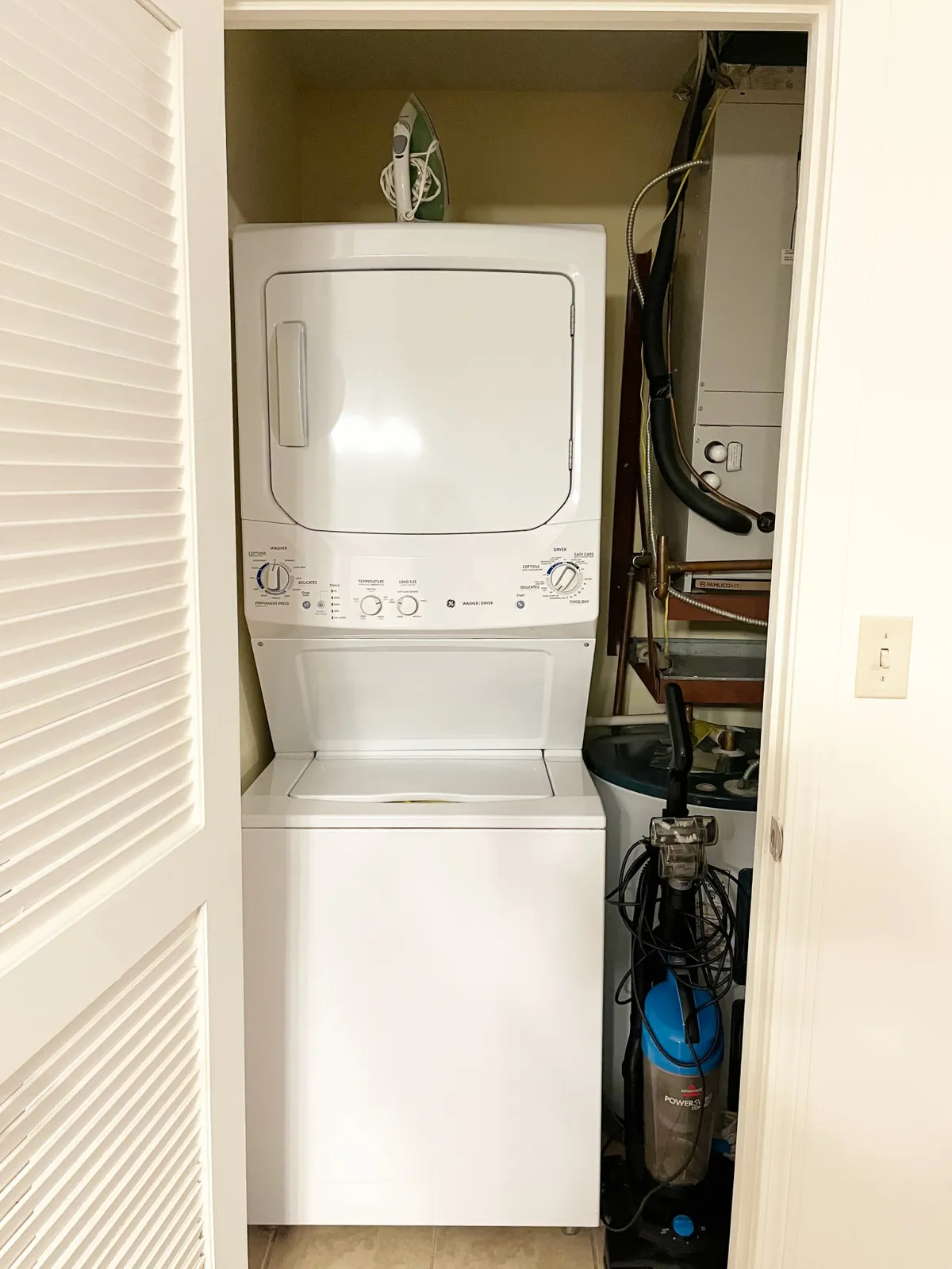 A practical laundry area featuring a washer, dryer, iron, and vacuum cleaner, neatly arranged to emphasize functionality and convenience for guests. The appliances are modern and accessible, set against a simple backdrop that highlights ease of use.
