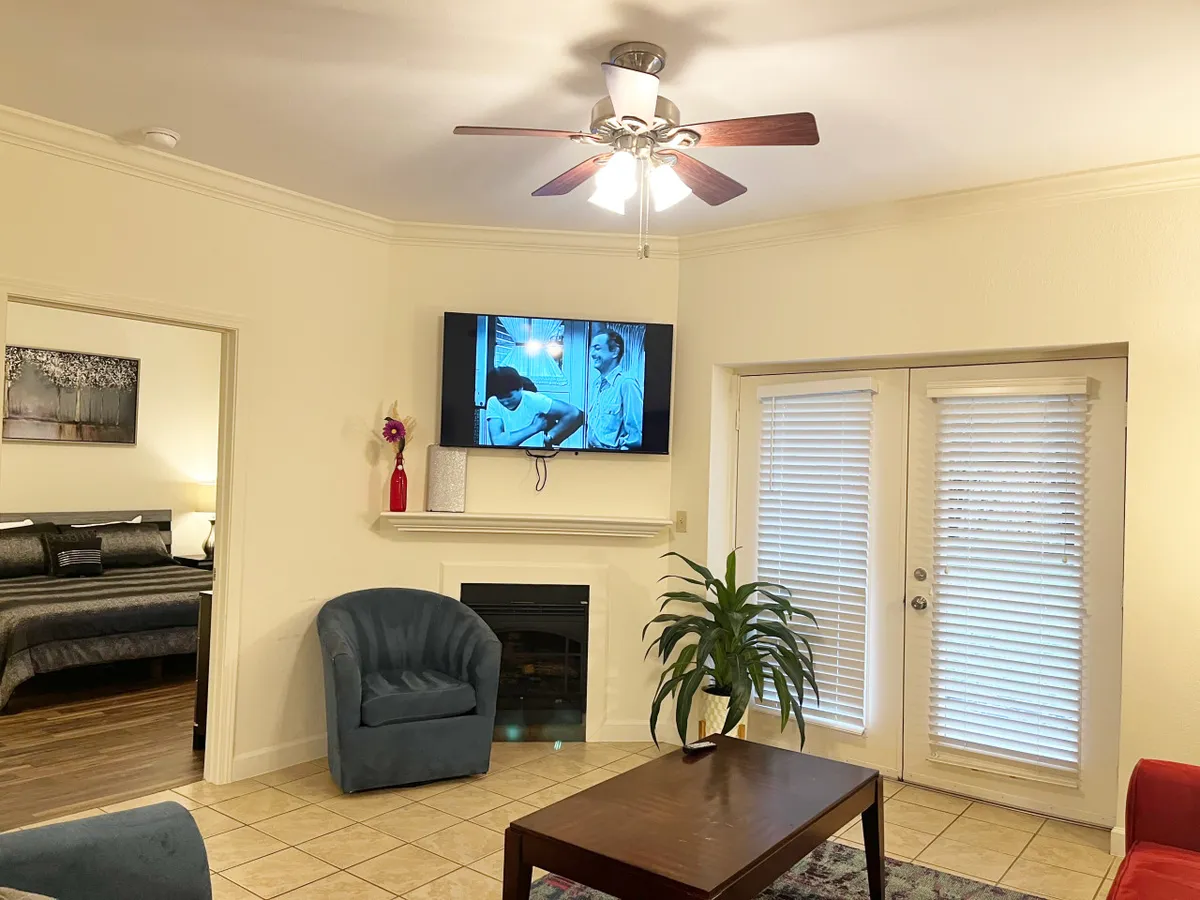 A cozy living room setup displaying a flat-screen TV showing a black-and-white movie, a blue chair positioned for comfortable viewing, a coffee table, a green plant adding a touch of nature, and a fireplace that anchors the space.