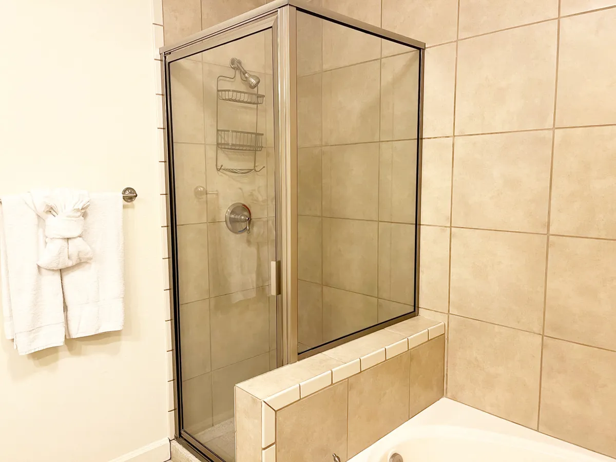A bright bathroom with a modern shower enclosure, a spacious bathtub, and a towel rack with neatly arranged towels. The clean, soothing design creates an inviting space for bathing and relaxation.